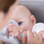 Adorable blue eyed baby looks at mom while breastfeeding
