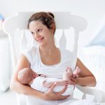 Young Mother And Newborn Baby In White Bedroom